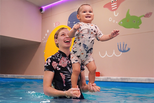 A person holding a baby in a pool

Description automatically generated