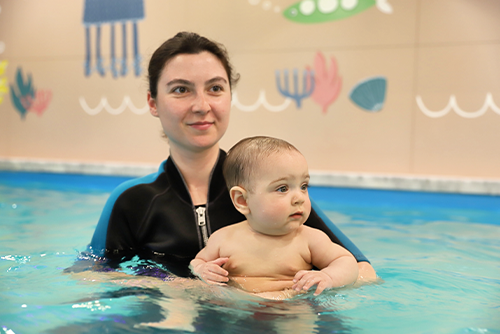 A person holding a baby in a pool

Description automatically generated